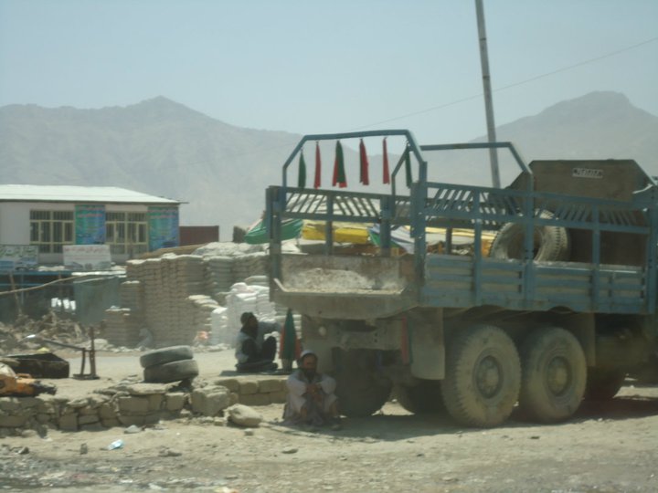 Man seeking shade under a truck (Company Road, near Arghandeh)